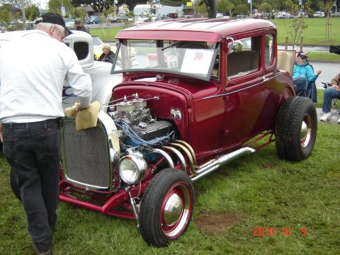 1993 Ford Bronco - A man polishes the front grille of a custom red hot rod coupe with a powerful V8 engine on display.