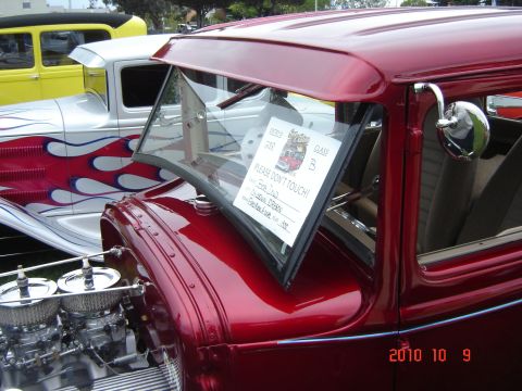 1993 Ford Bronco - A shiny red coupe is parked next to a silver car with flame graphics, with a sign on the windshield asking not to touch.