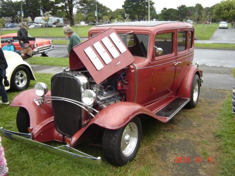 1993 Ford Bronco - A classic red sedan hot rod is displayed with its hood open, revealing the engine, while other vehicles are visible in the background.