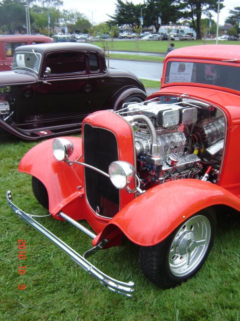 1993 Ford Bronco - Two classic hot rods displayed outdoors on a grassy area, one with its engine exposed.