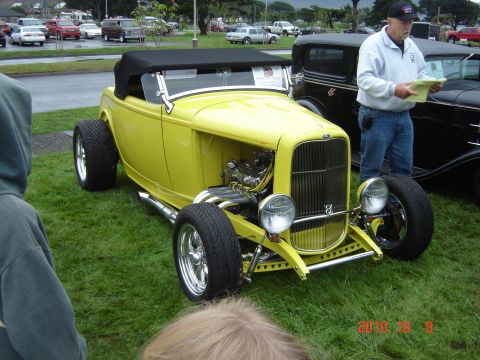1993 Ford Bronco - A man stands by a yellow hot rod convertible, holding some papers, while another car is parked beside it.
