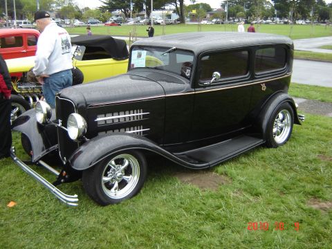 1993 Ford Bronco - A black sedan hot rod is parked on grass at an outdoor event with other vehicles in the background.