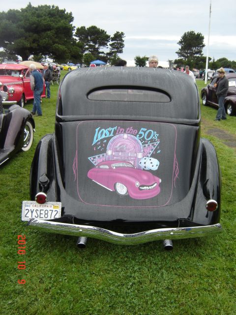 1993 Ford Bronco - A classic hot rod with a 'Lost in the 50s' mural is parked on a grassy field at an outdoor car show.