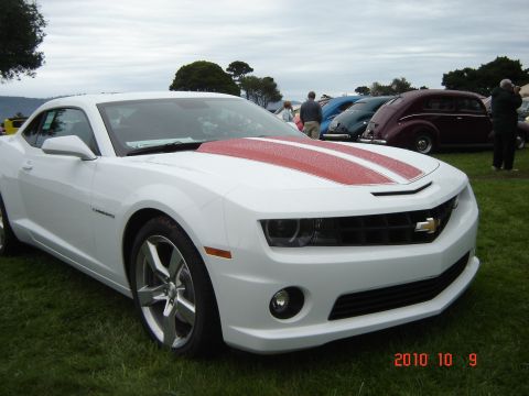 1993 Ford Bronco - A white Chevrolet Camaro with red racing stripes on the hood is parked on grass, with other vehicles in the background.