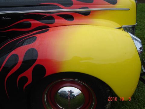 1993 Ford Bronco - A close-up of a car's fender shows custom flame paint and a chrome hubcap reflecting another vehicle.