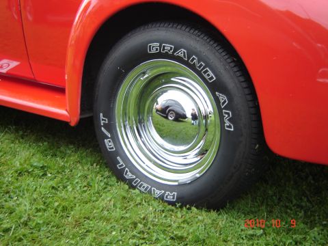 1993 Ford Bronco - A close-up of a shiny chrome wheel and tire on a red vehicle shows a reflection of another car and a person.