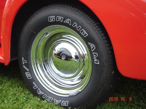 1993 Ford Bronco - A chrome hubcap on a red vehicle reflects a black car parked on grass.