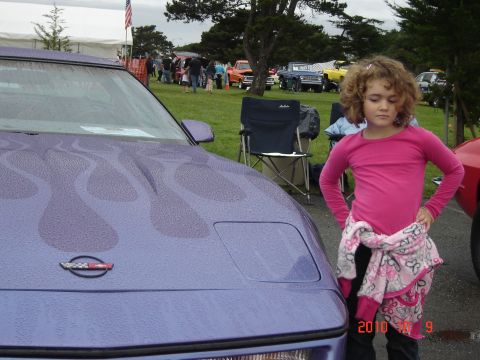 1993 Ford Bronco - A young girl stands next to a purple car with flame graphics at an outdoor car show.
