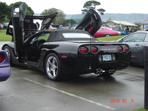 1993 Ford Bronco - A black Corvette with its doors open sits in a parking lot on a cloudy day.