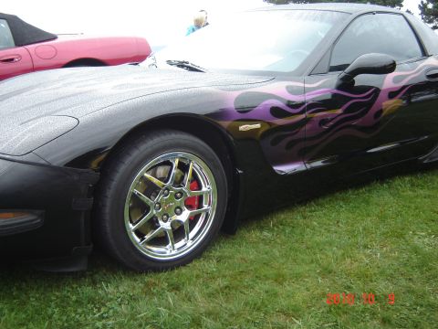 1993 Ford Bronco - A black sports car with custom purple flame graphics is parked on a grassy lawn next to a pink convertible.