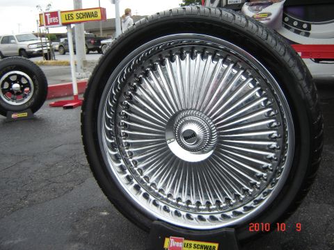 1993 Ford Bronco - A close-up of a custom chrome wire wheel is shown, with other vehicles and a Les Schwab Tires sign in the background.