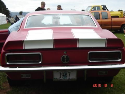 1993 Ford Bronco - Rear view of a red 1967 Chevrolet Camaro with racing stripes, parked outdoors with other vehicles.