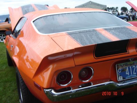 1993 Ford Bronco - A classic orange muscle car with racing stripes is parked on the grass, with another vehicle visible in the background.