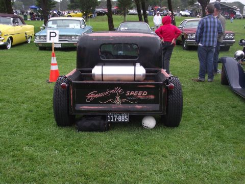1993 Ford Bronco - A custom rat rod pickup truck is displayed at an outdoor car show, a prominent fuel tank and vintage styling.
