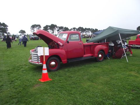 1993 Ford Bronco - A vintage red pickup truck is displayed with its hood open at an outdoor gathering, with other vehicles and tents in the background.