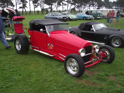 1993 Ford Bronco - A red hot rod is parked on a grassy field next to other vehicles.