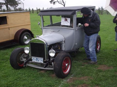 1993 Ford Bronco - A silver hot rod with red wheels is parked on grass, with a person standing by the driver's door.