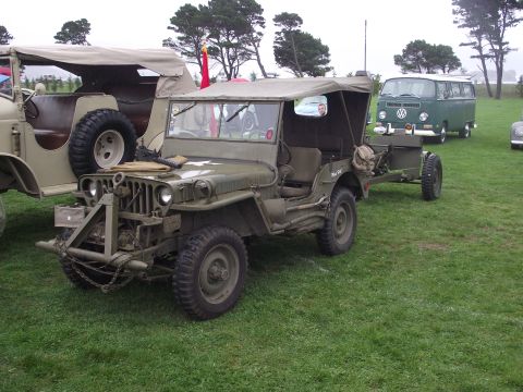 1993 Ford Bronco - A military jeep and a Volkswagen van parked on a grassy field under a cloudy sky.