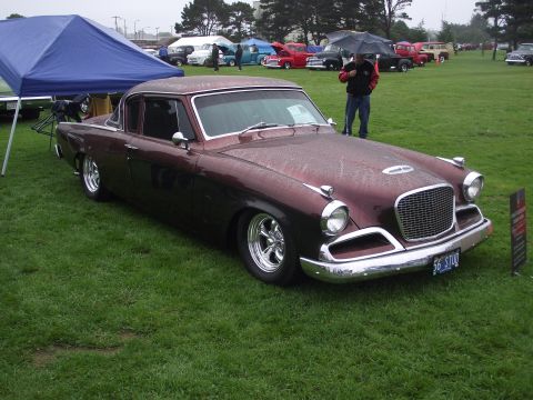 1993 Ford Bronco - A maroon 1956 Studebaker coupe with chrome accents and custom wheels is displayed on a grassy field, with other vehicles and tents in the b…