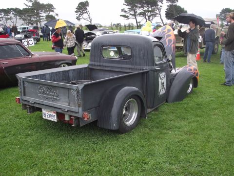 1993 Ford Bronco - A custom black pickup truck with flame graphics is parked on a grassy field with other vehicles and people.