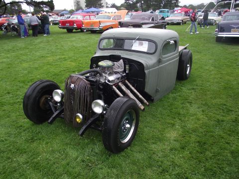 1993 Ford Bronco - A custom rat rod pickup truck is displayed on a grassy field alongside other vehicles.