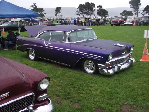 1993 Ford Bronco - A purple 1956 Chevrolet Bel Air is displayed at an outdoor car show with other vehicles and tents in the background.