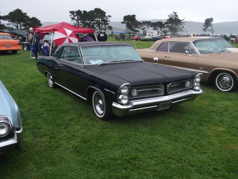 1993 Ford Bronco - A black 1963 Pontiac Grand Prix is parked on a grassy field next to other classic cars.