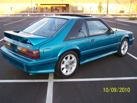 1995 Ford Bronco - A teal Ford Mustang is parked in a lot, showing its rear quarter panel and spoiler.