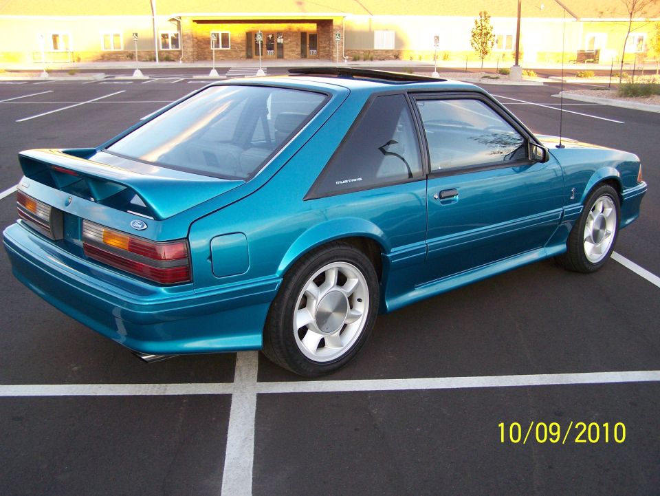 Teal Ford Mustang parked in a lot, rear quarter view
