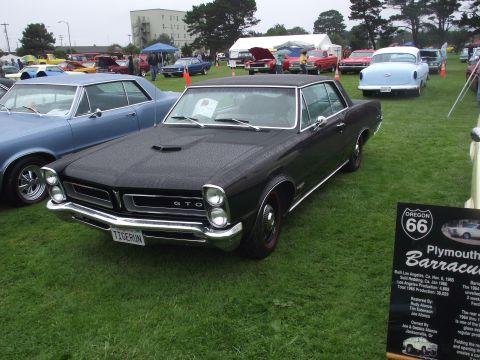 1993 Ford Bronco - A black 1965 Pontiac GTO is displayed at an outdoor car show next to a blue car.