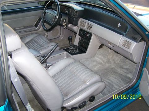 1995 Ford Bronco - The interior of a teal car features gray leather seats and a dashboard with a horse emblem.