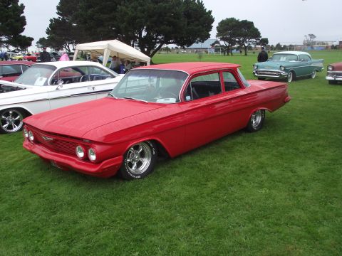 1993 Ford Bronco - A red 1961 Chevrolet sedan is displayed at an outdoor car show with other vehicles present.