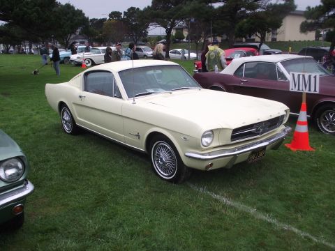 1993 Ford Bronco - A classic 1965 Ford Mustang Fastback is displayed at an outdoor event with other vehicles in the background.