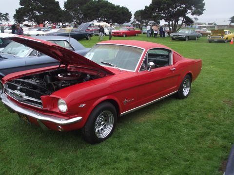 1993 Ford Bronco - A red 1965 Ford Mustang coupe is displayed with its hood up at an outdoor car event.