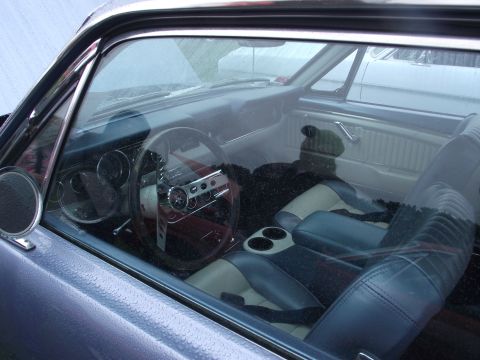 1993 Ford Bronco - Interior of a classic two-door coupe shot through the rain-beaded driver's window, showing two-tone black and cream bucket seats, a center…