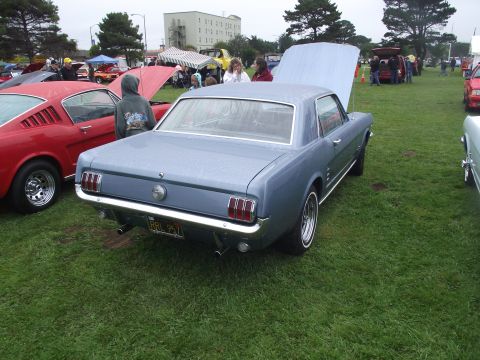 1993 Ford Bronco - Three-quarter rear view of a light blue 1966 Ford Mustang hardtop on wet grass at an outdoor car show, hood propped open, wearing chrome fi…