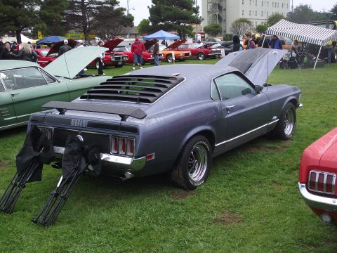 1993 Ford Bronco - Rear three-quarter view of a grey 1970 Ford Mustang Mach 1 SportsRoof at an outdoor grass car show, water-beaded from drizzle, with rear wi…
