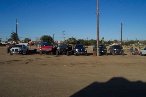 1995 Ford Bronco - A collection of modified trucks and SUVs are parked in an outdoor lot on a sunny day.