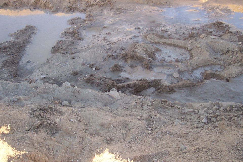 Muddy ground with visible tire tracks and standing water
