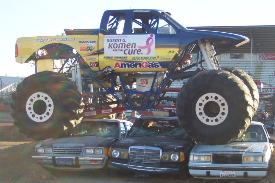 Monster truck with 'Susan G. Komen for the Cure' logo crushing several cars