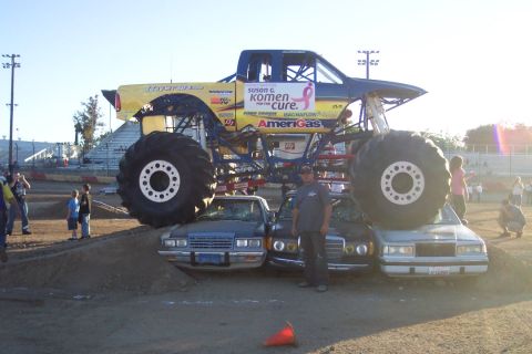 1995 Ford Bronco - A monster truck is positioned over several crushed cars on a dirt track with spectators in the background.