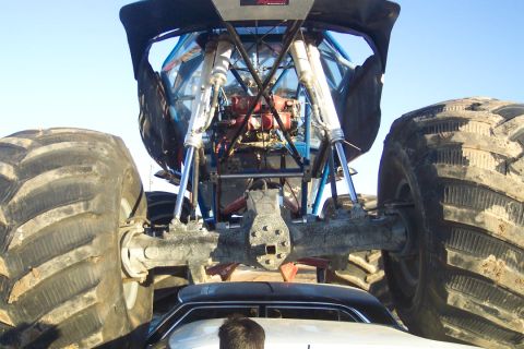 1995 Ford Bronco - A monster truck is positioned directly behind a car, obscuring most of the car from view.