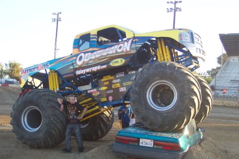1995 Ford Bronco - A monster truck crushes a car in an arena, with spectators in the stands.