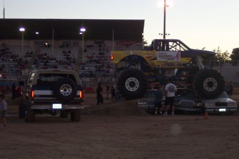 1995 Ford Bronco - A tan Ford Bronco is parked on dirt in front of stadium seating, with a monster truck nearby.