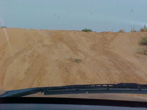 1989 Ford Bronco - Driving through a sandy terrain, the view from the windshield shows a hill with tire tracks.