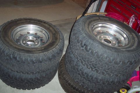 1995 Ford Bronco - A set of four off-road tires with chrome rims are stacked in a garage, with a red toolbox visible in the background.