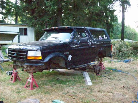 1995 Ford Bronco - A black Ford Bronco is elevated on jack stands with its front end partially dismantled in an outdoor setting.