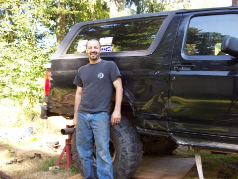 1995 Ford Bronco - A man poses next to a heavily modified black SUV, which appears to be undergoing some work.