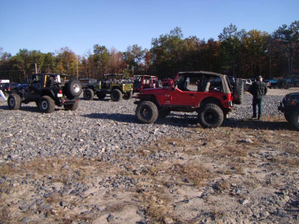 Red lifted Jeep Wrangler with folded soft top on gravel lot with other Jeeps