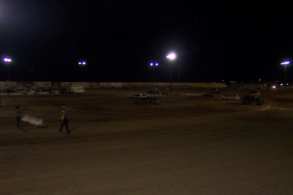Dirt track at night with lights, vehicles, and people